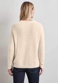 Cremfarbener Strickpullover mit lockerer Passform. Verfügt über lange Ärmel, weiche Textur und einen runden Ausschnitt. Kombiniert mit dunklen Jeans.