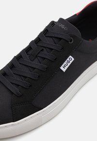 Svarta syntetiska sneakers med en texturerad ovansida, tonade snören, vit logotagg och vit gummisula. Med kontrasterande innersula.