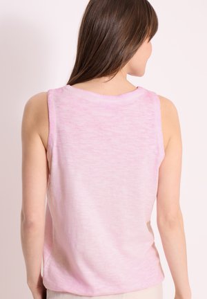 Vrouw met lang bruin haar draagt een mouwloze lichtroze top, gezien van achteren tegen een effen bleke achtergrond.