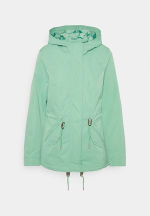 Lichtgroene capuchonjas met voorrits, verstelbare taillekoorden en klepzakken op een witte achtergrond.