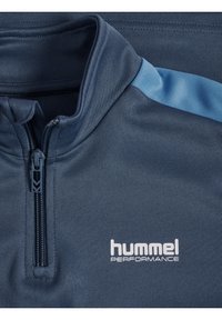 Veste de sport zippée bleu marine en tissu texturé avec un accent bleu clair sur l'épaule et le logo "hummel PERFORMANCE" en blanc.