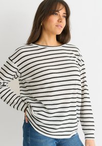 Black and white striped knit sweater with long sleeves, round neckline, and a relaxed fit, paired with blue denim. Textured fabric.