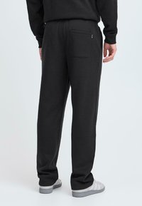 Sorte sweatpants med snørre i taljen, tætsiddende ben og en baglomme; lavet af blødt stof med en glat overflade.