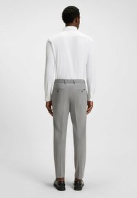 Chemise blanche à manches longues avec col, assortie à un pantalon tailleur gris clair doté de deux poches arrière et d'une texture subtile. Chaussures noires.