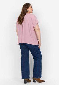 Top rosa chiaro a maniche corte con una vestibilità comoda, abbinato a jeans dritti blu scuro e stivaletti con tacco marroni.