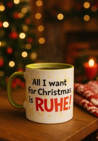 White ceramic mug with a green handle, featuring a colorful design that reads "All I want for Christmas is RUHE!" against holiday-themed accents.