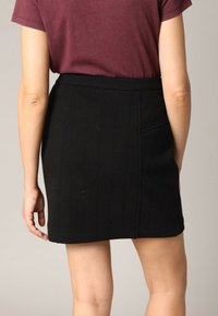 Mini-jupe noire en tissu texturé, dotée d'une taille haute et de poches latérales. Le dos présente des détails de couture verticaux.