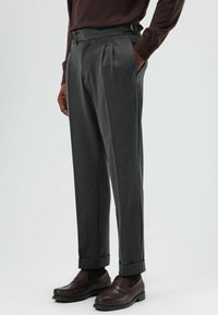 Donkergrijze geplooide broek met een hoge taille en verstelbare riemlussen, gecombineerd met bruine leren loafers, die een gladde textuur tonen.