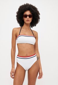 Hvit bikini med bandeau-top og høyt liv på bunnen. Har røde og marineblå striper langs kantene. Glatt, elastisk materiale.