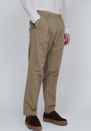 Pantaloni ușori, de culoare bej, cu talie elastică, buzunare laterale și o textură fină, asortați cu pantofi maro.