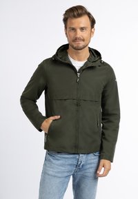 Herreur i olivengrøn letvægtsjakke med hætte, der har en lynlåsslukning, sidelommer og en glat tekstur. Sammen med lyseblå jeans.