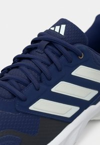Chaussures de sport bleu marine avec une tige en mesh texturé, des bandes blanches et une semelle en caoutchouc. Les lacets sont bleu foncé et conçus pour un maintien structuré.