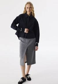 Camicia blu navy con maniche lunghe, abbinata a una gonna a tubino grigia fino al ginocchio con uno spacco laterale. Sneakers nere con dettagli bianchi.