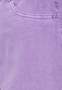 Tessuto denim viola con una texture sottile, caratterizzato da una tasca e dettagli di cuciture visibili in una tonalità di viola più scura.