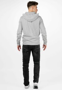 Grijze hoodie met een capuchon en lange mouwen, gecombineerd met zwarte jeans met contrasterende stiksels, en witte sneakers met merklogo.