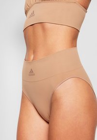 Beige Sport-Bralette und hochgeschnittene Panties aus glattem, dehnbarem Stoff mit subtiler Glanzoptik, ausgestattet mit einem Logo auf dem Bund.
