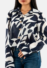 Camisa de botones con un patrón abstracto en azul marino y blanco, de mangas largas, con cuello y botones de madera, hecha de una tela ligera.