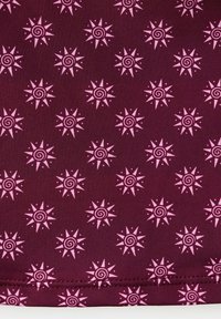 Tissu bordeaux avec un motif répétitif de soleils roses aux centres en spirale et aux huit rayons pointus.