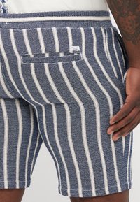 Stripede shorts i navy og hvidt stof. Har en elastisk talje og en baglomme med et mærke. Teksturert, vævet stof.