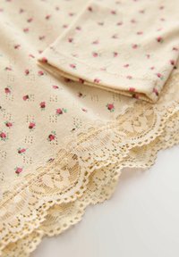 Beige stof med lille pink blomsterprint og dekorativ blondekant langs kanten på en flad overflade.