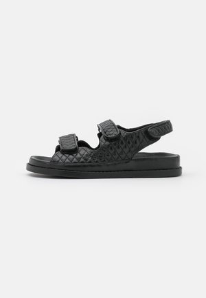 Black sandals with a quilted texture, featuring two adjustable Velcro straps, open toe, and a cushioned flat sole.