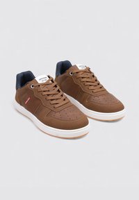 Baskets en daim marron avec un bout perforé, des côtés texturés, une semelle en caoutchouc blanc et des accents bleu marine sur le col. Présente un design à lacets.