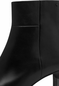 Bottine en cuir noir avec une silhouette élégante, présentant une texture lisse et un détail de couture minimaliste. Comprend un design à talon haut.