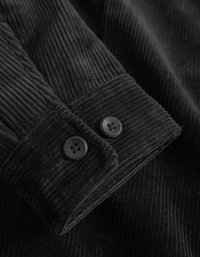 Μαύρο πανί κορντούρας με έντονες ραβδώσεις. Ο κορμός διαθέτει δύο μαύρα κουμπιά και καθαρή τελείωση, αναδεικνύοντας την υφή και τις λεπτομέρειες.