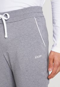 Grå joggebukser laget av myk stoff med snor i livet, hvite detaljer og et brodert "JOOP!"-logo på siden.