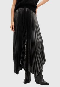 Black pleated skirt made of glossy fabric, featuring a high waist and asymmetrical hem, paired with knee-high black boots.