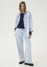 Ljusblå denimskjorta i oversize med ficka fram, ihop med matchande vida jeans. Svarta skor fulländar outfiten.