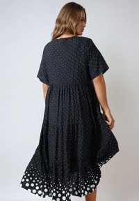 Zwarte jurk met witte stippen, ronde halslijn, korte mouwen en een gelaagde rokontwerp met grotere witte stippen aan de zoom.
