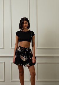 Top cropped preto com mangas curtas, emparelhado com uma saia preta com padrão floral e um laço na cintura. Tecido leve e corte descontraído.