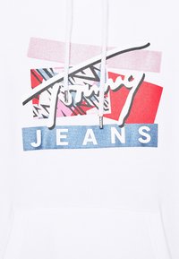 Biała bluza z kapturem z wielokolorowym graficznym wzorem z napisem "Tommy Jeans" w odważnych niebieskich literach na denimu w tle oraz wzorzystymi akcentami.