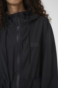 Must kerge jope kapuutsiga, millel on esikinnitus tõmblukuga, nöör ja elastne vöökoht. Minimalistlik disain logodega aktsendiga.