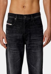 Jeans de mezclilla negra con corte recto, costuras visibles y un pequeño detalle de bolsillo. La tela tiene una textura ligeramente desgastada.