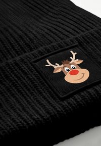 Black knitted beanie with a textured pattern and a square patch featuring a smiling reindeer face, complete with antlers and a red nose.