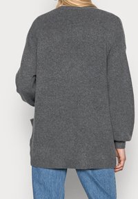 Grauer Strickpullover mit einem lockeren Schnitt, langen Ärmeln und Rippenbündchen. Die Rückseite zeigt ein einfaches Design ohne zusätzliche Details.