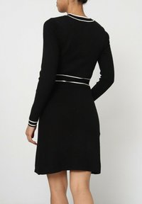 Robe noire à manches longues, avec un bord blanc le long de l'encolure et des poignets, corsage ajusté, jupe évasée, confectionnée en matière tricot douce.