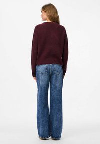 Burgundijas adīts džemperis ar brīvu piegriezumu, apaļu dekoltē un garām piedurknēm. Apvienots ar platām zila džinsa biksēm ar aizmugurējām kabatām.