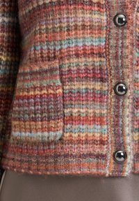 Close-up of multicolored knit cardigan with patch pocket and three shiny black buttons over smooth brown fabric.
