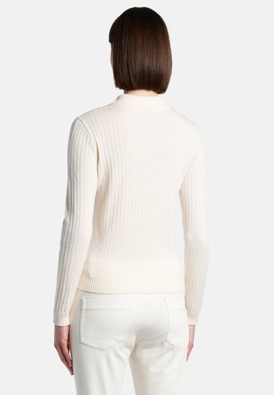 Geripptes cremefarbenes Sweatshirt mit langen Ärmeln und rundem Ausschnitt, das eine eng anliegende Passform und eine strukturierte Oberfläche aufweist, kombiniert mit weißen Hosen.