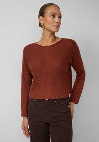 Rustfarbener Strickpullover mit Rundhalsausschnitt und langen Ärmeln, kombiniert mit dunkelpurpurfarbenen Jeans. Angenehme Textur, cropped Design.