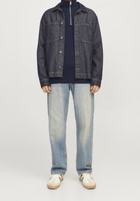 Veste en jean bleu foncé avec fermetures à boutons, associée à un pull côtelé bleu marine et un jean ample bleu clair. Baskets blanches avec des touches de vert.
