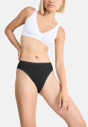 Zwarte hooggegraafde slip met kantafwerking. Zachte stretchstof en een gladde, aansluitende pasvorm. Past bij een witte draadloze beha.