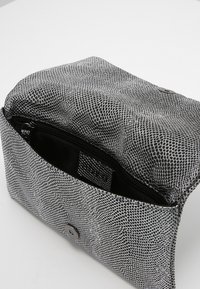 Czarnobiała teksturowana saszetka z wzorem skóry węża, wyposażona w czarny zamek błyskawiczny, srebrne zapięcie na guzik oraz wewnętrzną kieszeń.