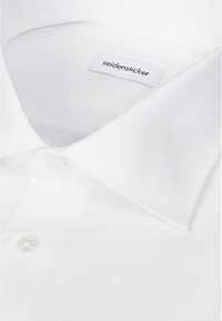 Gros plan sur le col et les boutons supérieurs d'une chemise blanche avec une étiquette visible indiquant "seidensticker."