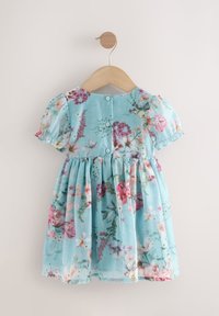 Robe bleue claire pour tout-petit avec manches bouffantes, imprimé floral et boutons dans le dos, suspendue à un cintre en bois contre un mur beige.