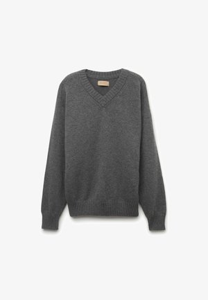 Pull en gris tricoté avec un design à col en V, des poignets et un ourlet côtelés, et une texture douce. Tissu léger idéal pour le superposition.