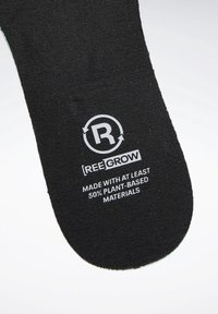 Étiquette en tissu noire avec le texte « REEGROW » et « Fabriqué avec au moins 50 % de matériaux d'origine végétale » imprimés en blanc.